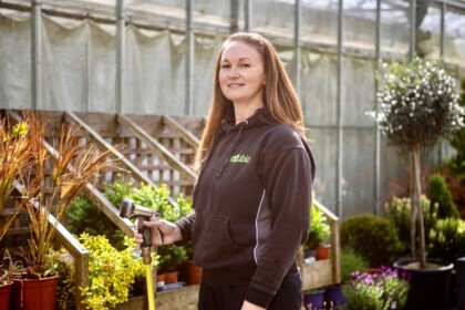 Female HortiCare technician using a spray hose to water interior plants within a commercial environment.