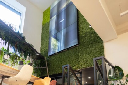 Large preserved moss wall with integrated digital display, surrounded by hanging plants and contemporary furniture at Exubia's London showroom.