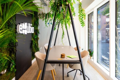 Contemporary meeting table beneath cascading hanging plants, with a green wall and Exubia branding at the London showroom.