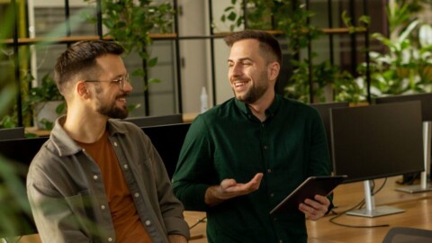 Two men leaning on a desk within a heavily planted office environment.